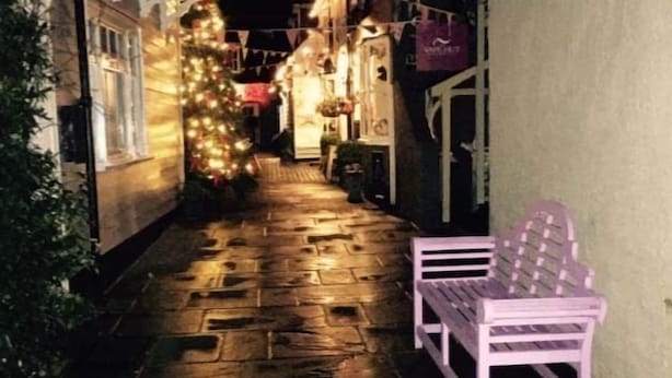 Een smalle steeg met een bank, lichtslingers en een kerstboom.