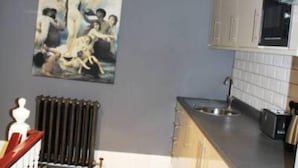Een keuken met een magnetron, fornuis en wastafel. Er hangt een schilderij aan de muur en er is een radiator.