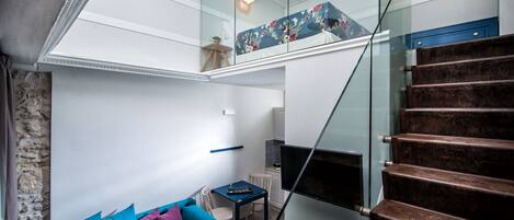 Un interior moderno con una escalera, un sofá con cojines, un televisor y una barandilla de cristal.