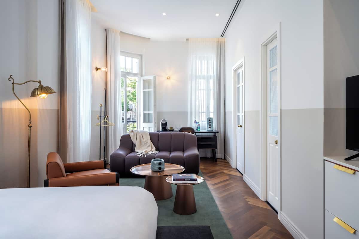 A modern hotel room with a large bed, a sofa, a coffee table, and a desk area.