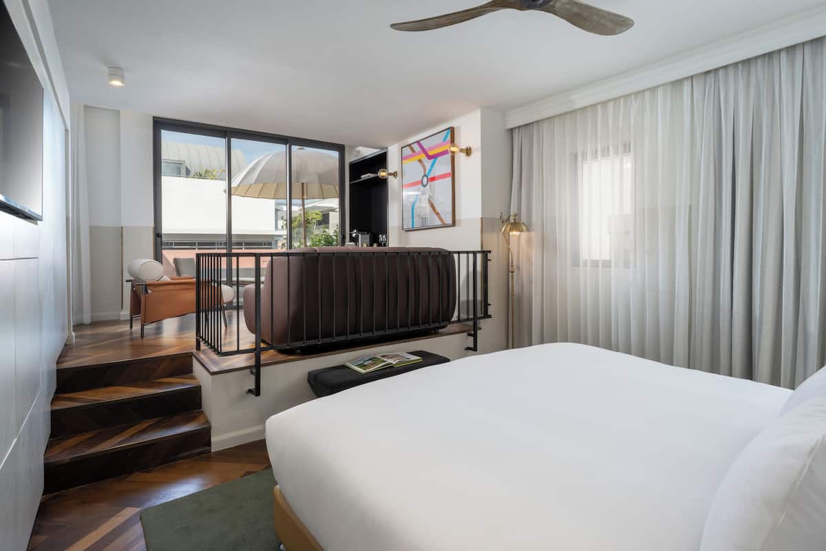 A hotel room with a large bed, a balcony with a view, a desk, and a chair.