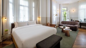 Une chambre d’hôtel avec un grand lit, deux canapés, une table basse, un bureau et une vue sur la verdure.