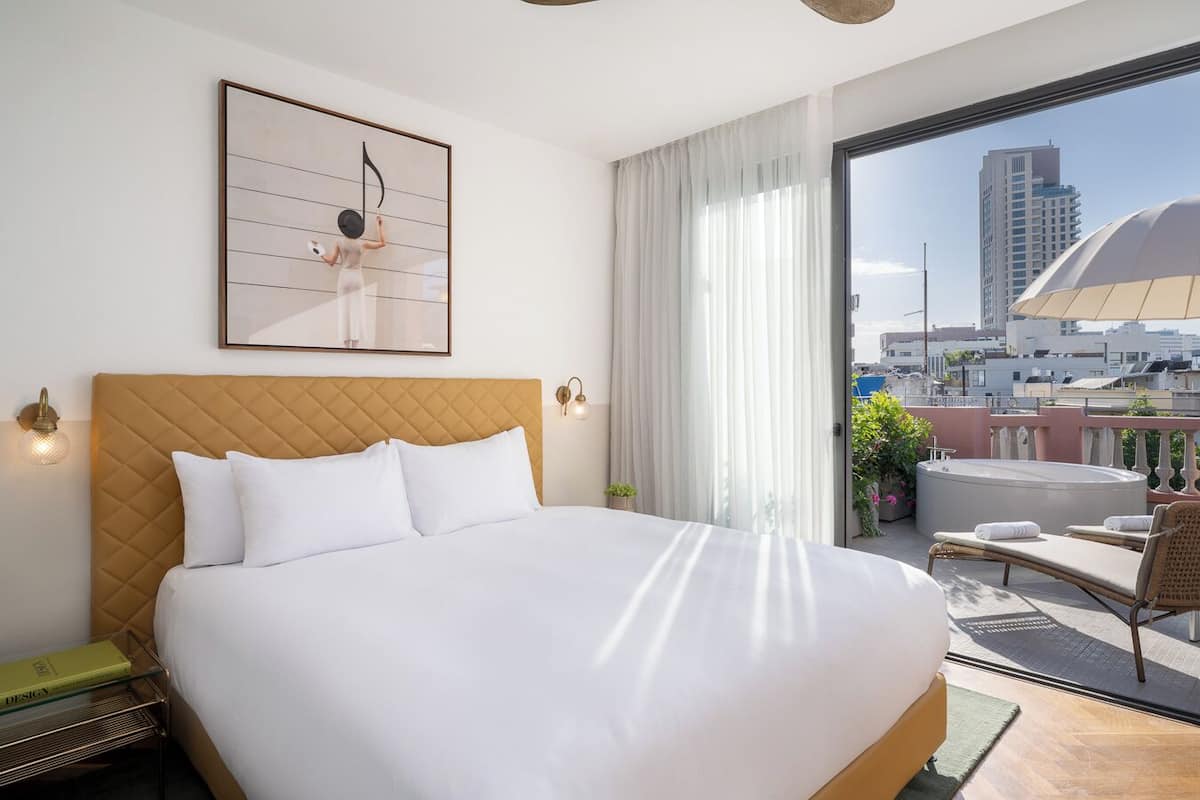 A hotel room with a large bed, a view of the city, and a balcony with outdoor furniture.