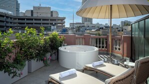 Une terrasse sur le toit équipée d’un jacuzzi, de chaises longues et d’un grand parasol.