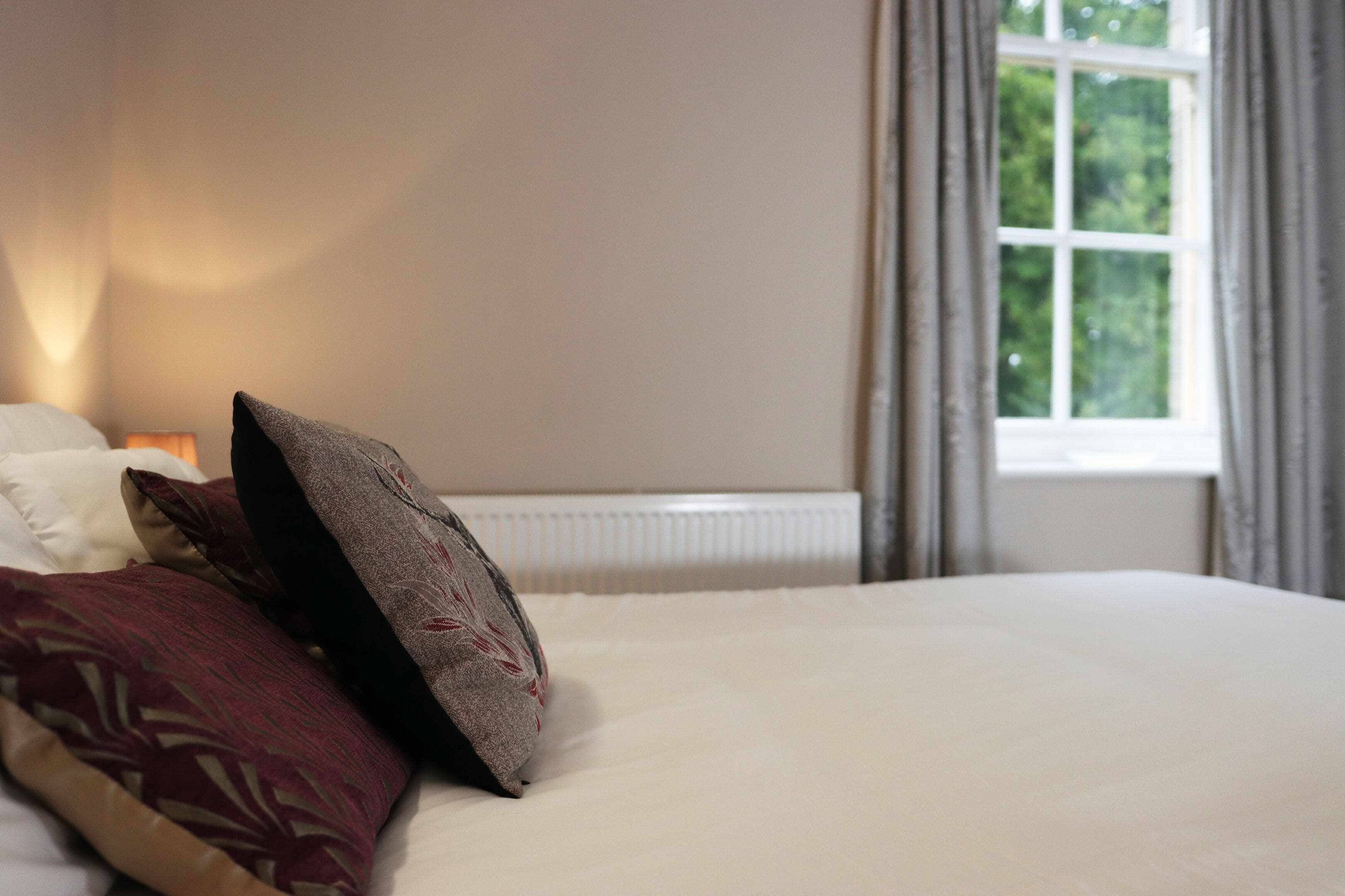 Ein ordentlich gemachtes Bett mit einer weißen Decke und mehreren Kissen, darunter eines mit Muster.