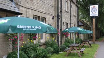 A building with a sign reading "TOLLEMACHE ARMS" and outdoor seating with "GREENE KING" umbrellas.