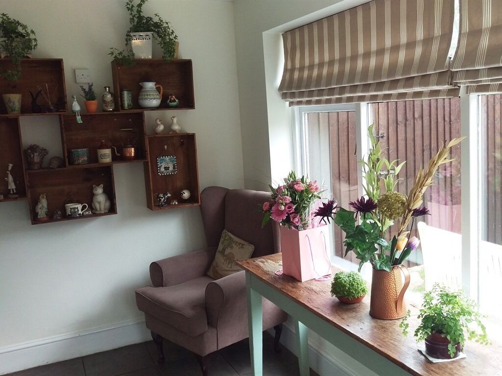 Una sala de estar acogedora con un sofá rosa, estanterías de madera con varios objetos decorativos y un ventanal con persiana a rayas.