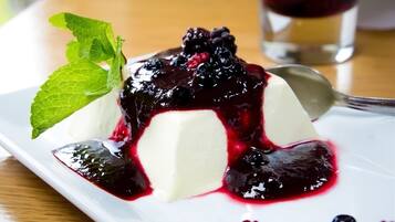 Panna cotta servie avec une compote de fruits rouges et décorée de feuilles de menthe, le tout présenté sur une assiette blanche.