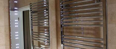 A bathroom with a chrome towel rack and a mirror reflecting lights.