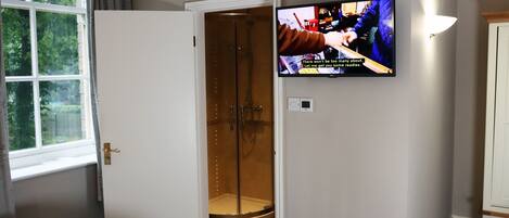 A hotel room with a bed, a TV mounted on the wall, a shower area, and a window with curtains.