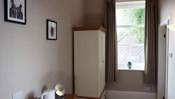 Una habitación con un armario blanco, una mesita con una tetera y dos cuadros en la pared.