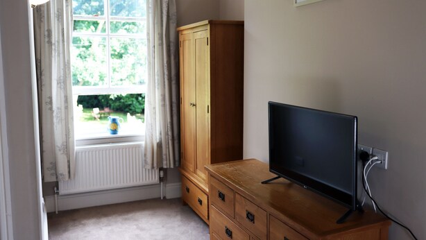 A room with a wooden cabinet, a television on top, a window with curtains, and a radiator.