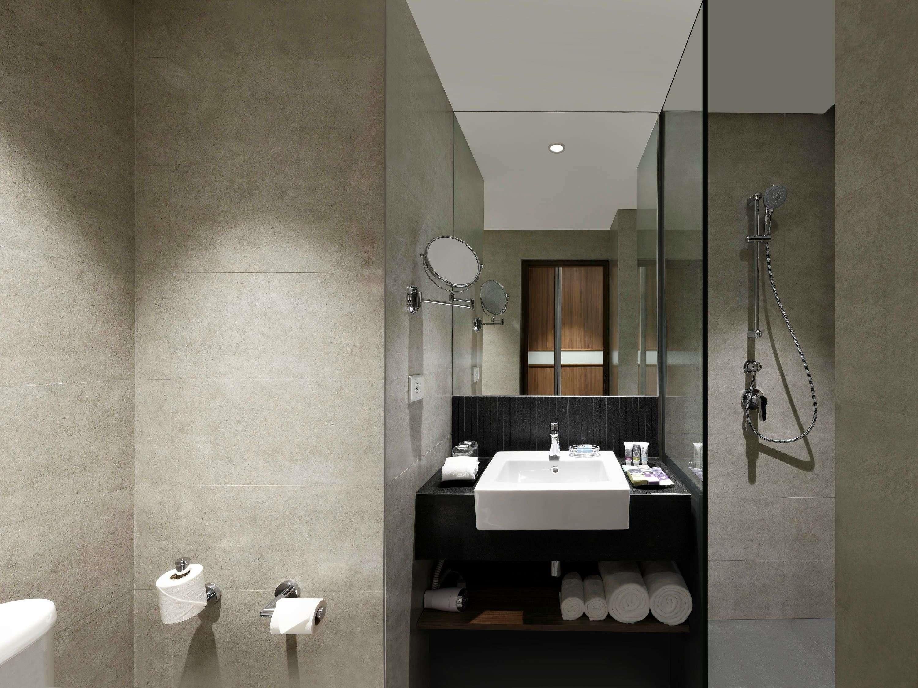 A modern bathroom with a large mirror, a sink, a shower, and a toilet.