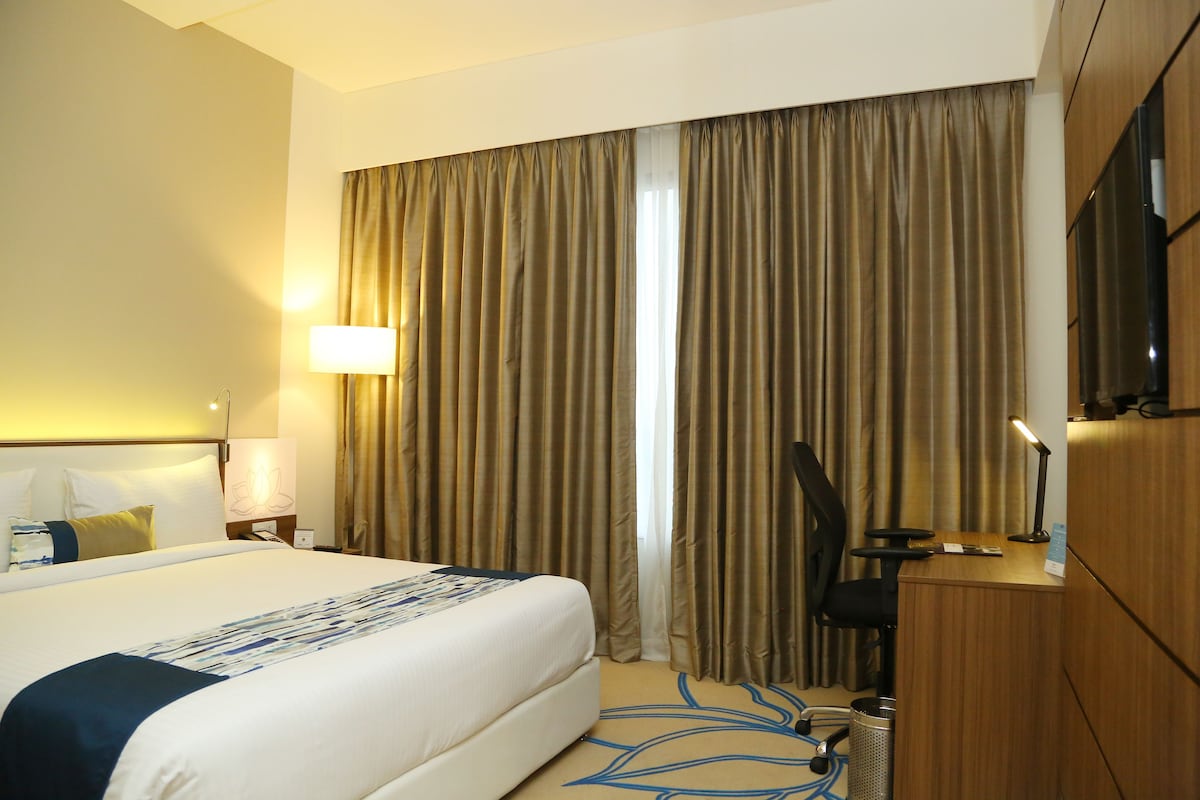 A hotel room with a large bed, a desk, a chair, and a TV.
