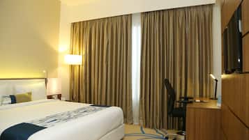 A hotel room with a large bed, a desk, a chair, and a TV.