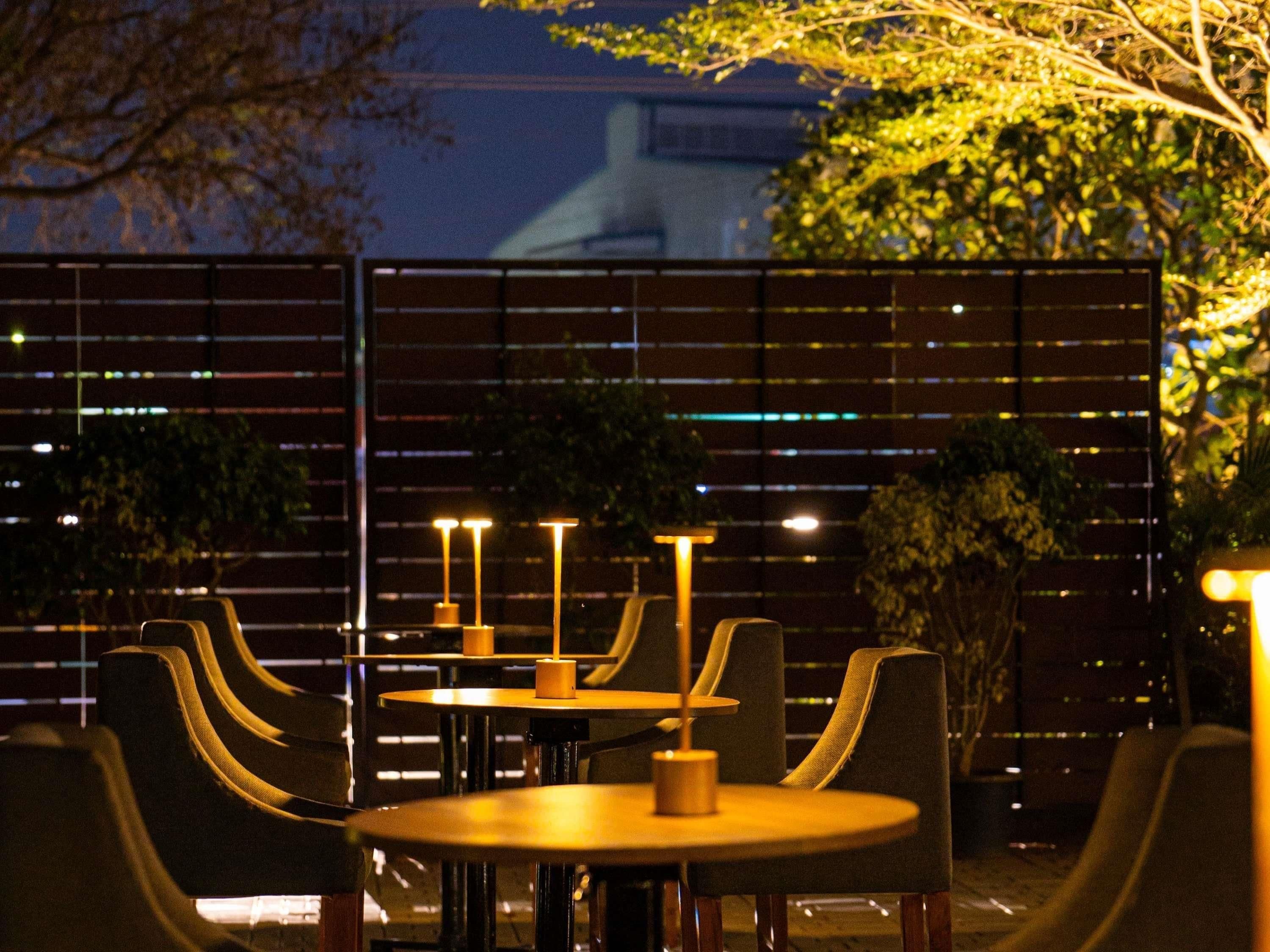 A dining area with tables and chairs, a fence, and a building in the background.