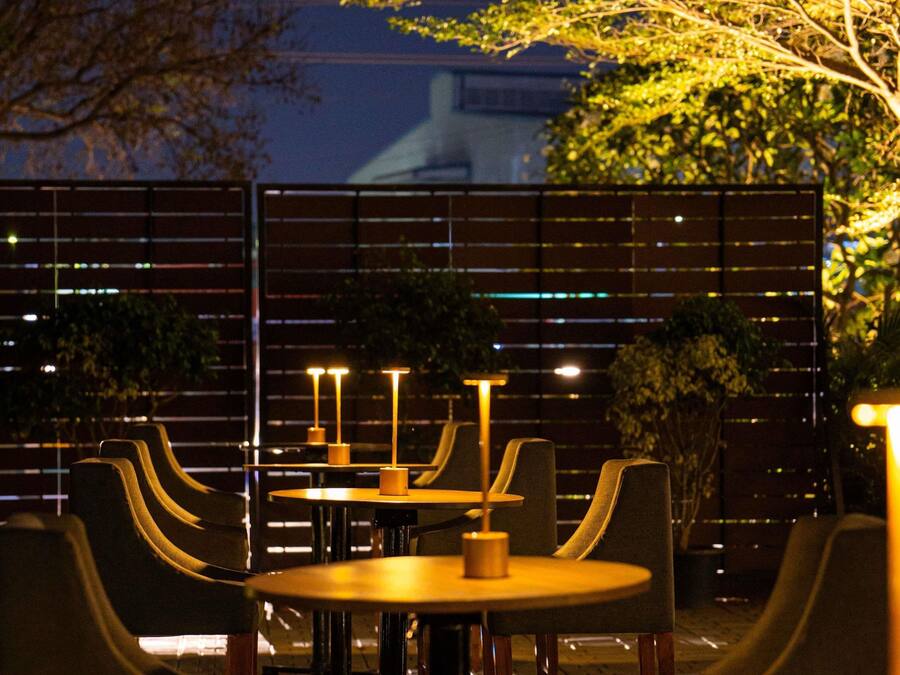 A dining area with tables and chairs, a fence, and a building in the background.