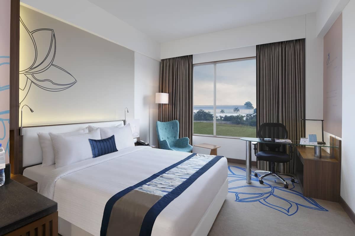 Ein Hotelzimmer mit einem großen Bett, einem Schreibtisch, einem Sessel und einer Aussicht ins Freie.
