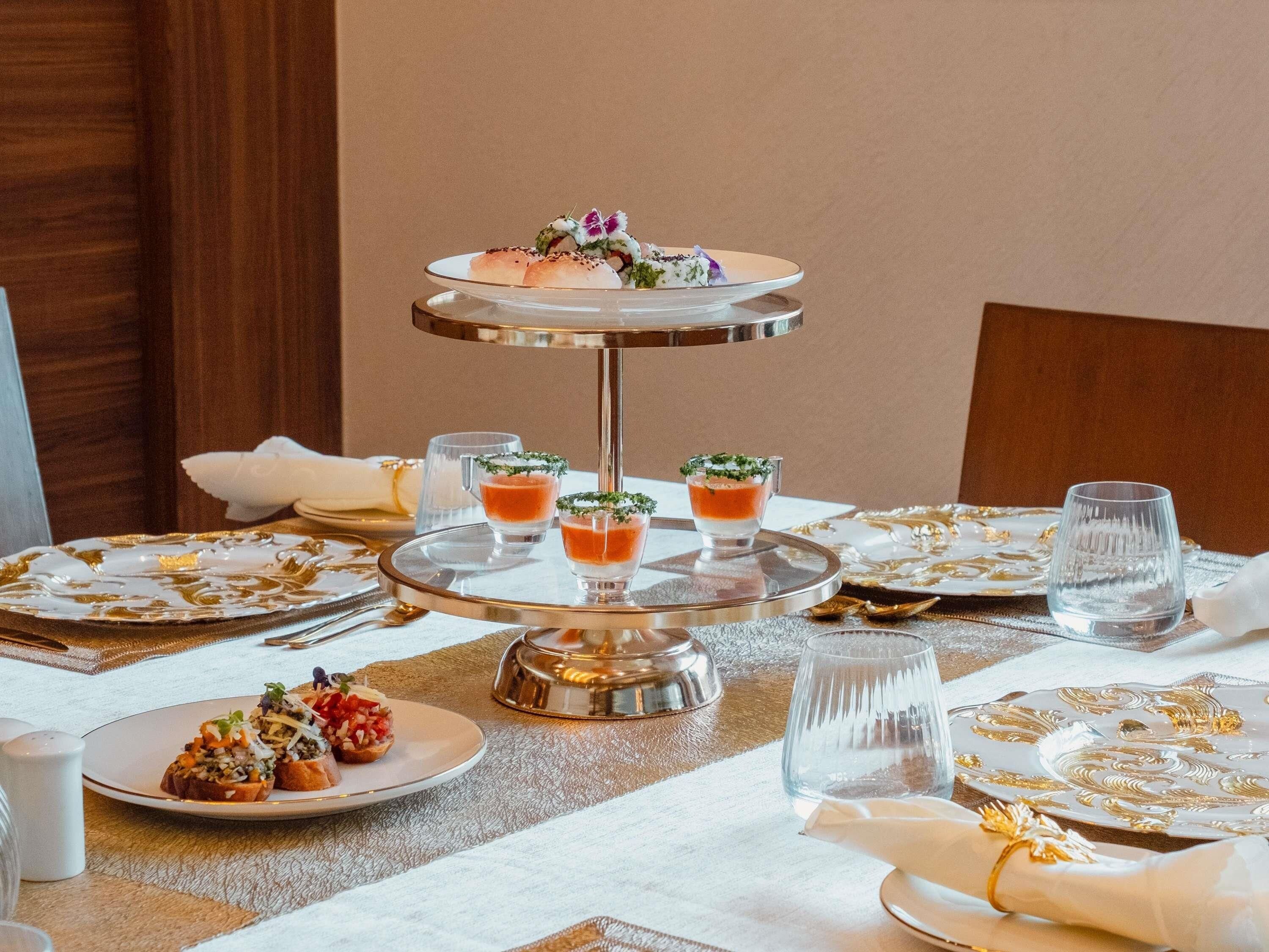 A three-tiered dessert stand with small glasses of dessert, a white plate with food, and a glass of water on a table.