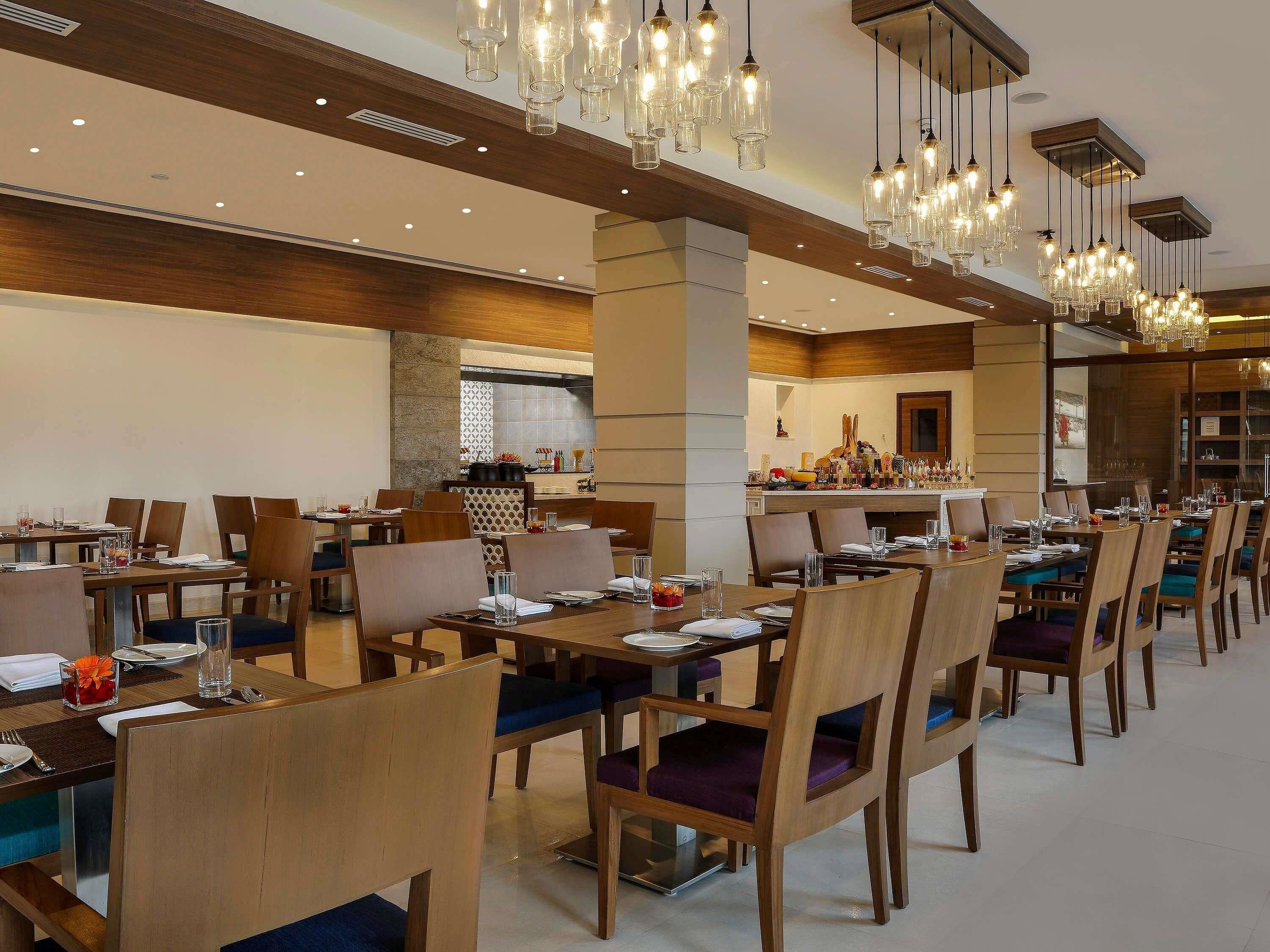 A spacious dining area with multiple tables, chairs, and hanging light fixtures.