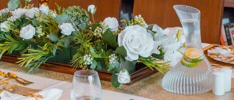 A table set with white tablecloths, gold leaf designs, and a centerpiece of white flowers.