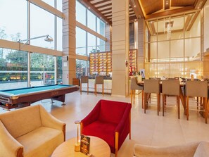 A pool table, bar area, and seating in a well-lit indoor space with large windows.