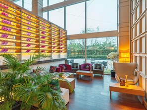 A spacious lobby with a large window, a wall of illuminated shelves, and several seating areas.