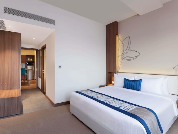 A hotel room with a large bed, a wooden wardrobe, a kitchenette, and a wall-mounted artwork.