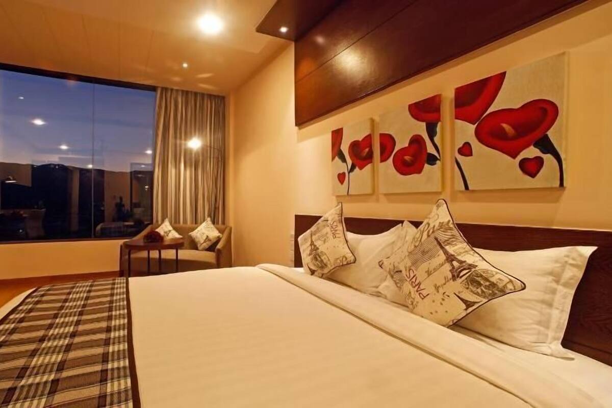 Een hotelkamer met een groot bed, uitzicht op de stad en een raam met gordijnen.