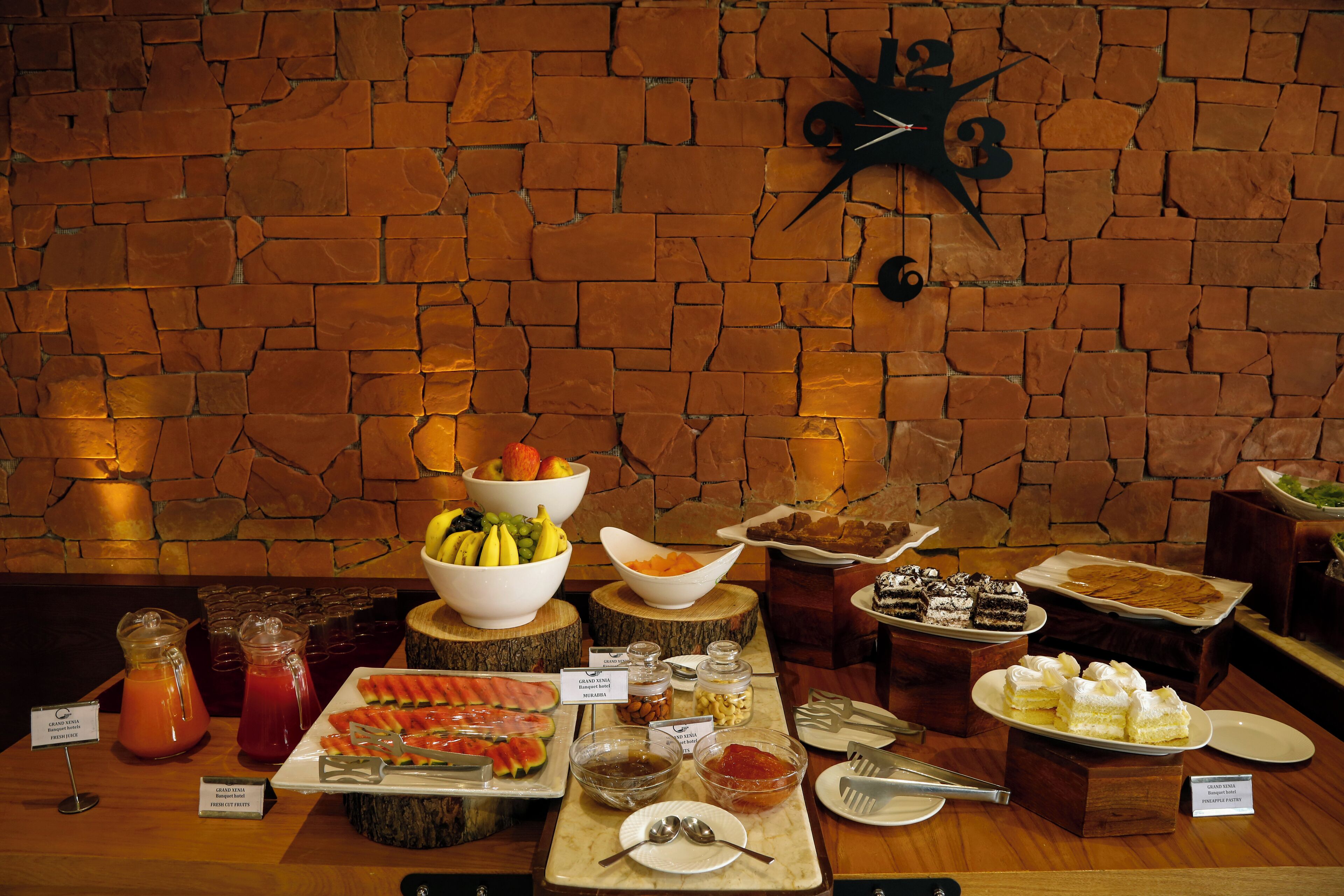 A buffet with various food items and beverages, set against a brick wall background.