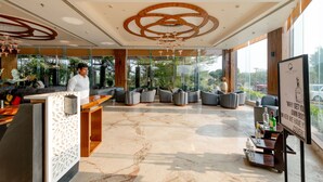 Un vestíbulo de hotel con una recepción, zona de estar y grandes ventanales que ofrecen vistas al exterior.