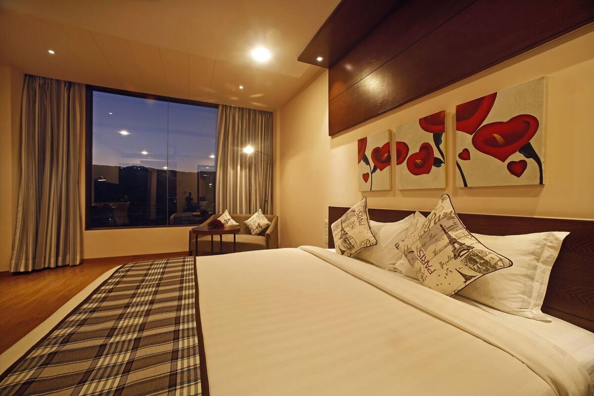 Een hotelkamer met een groot bed, een klein tafeltje, een bank en uitzicht op de stad door het raam.