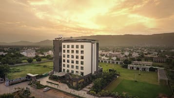 Un hotel moderno con un patio central, rodeado de abundante vegetación y vistas a un horizonte urbano distante.