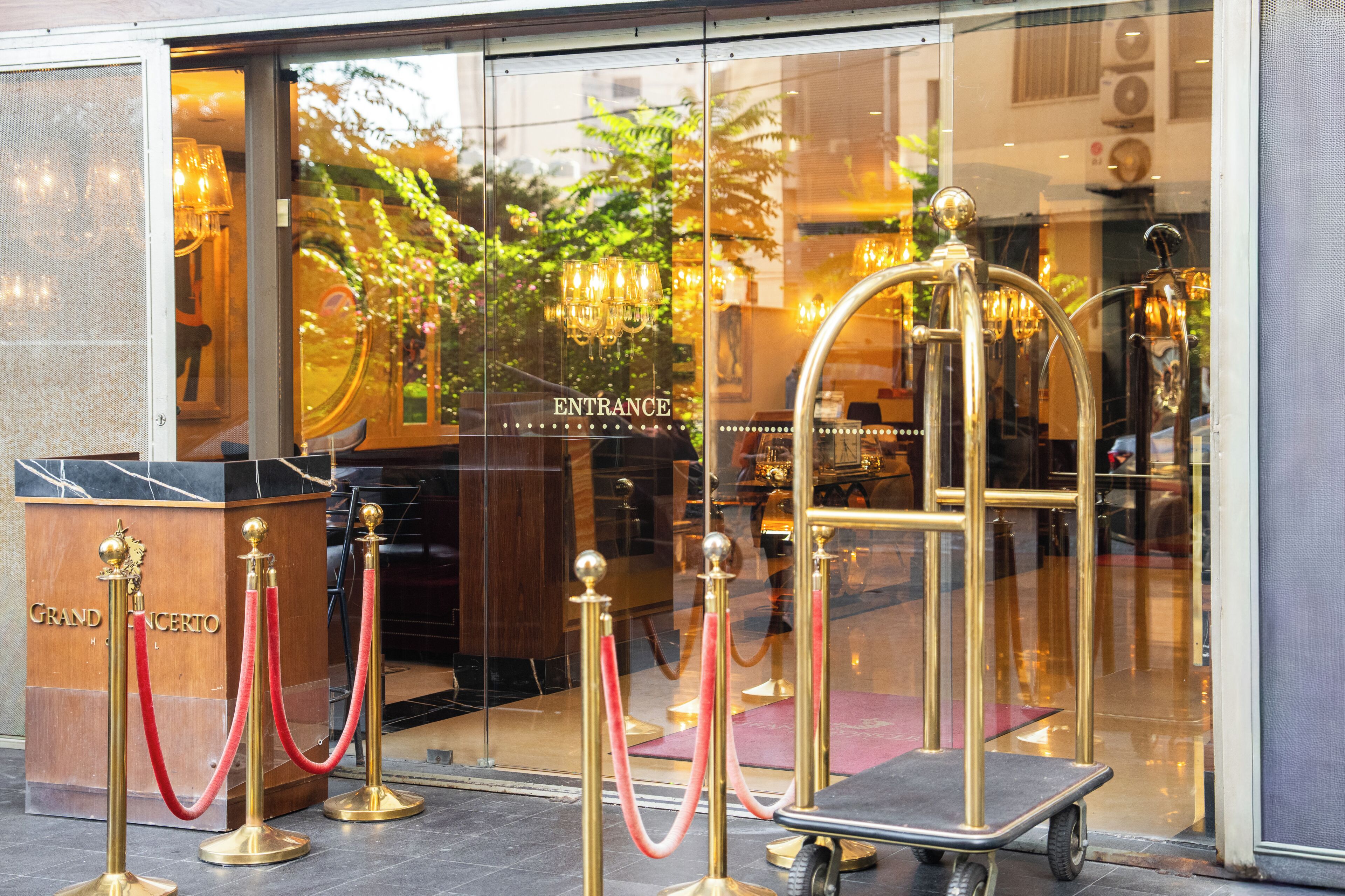 A hotel entrance with a glass door, a red carpet, and a gold-colored reception desk.