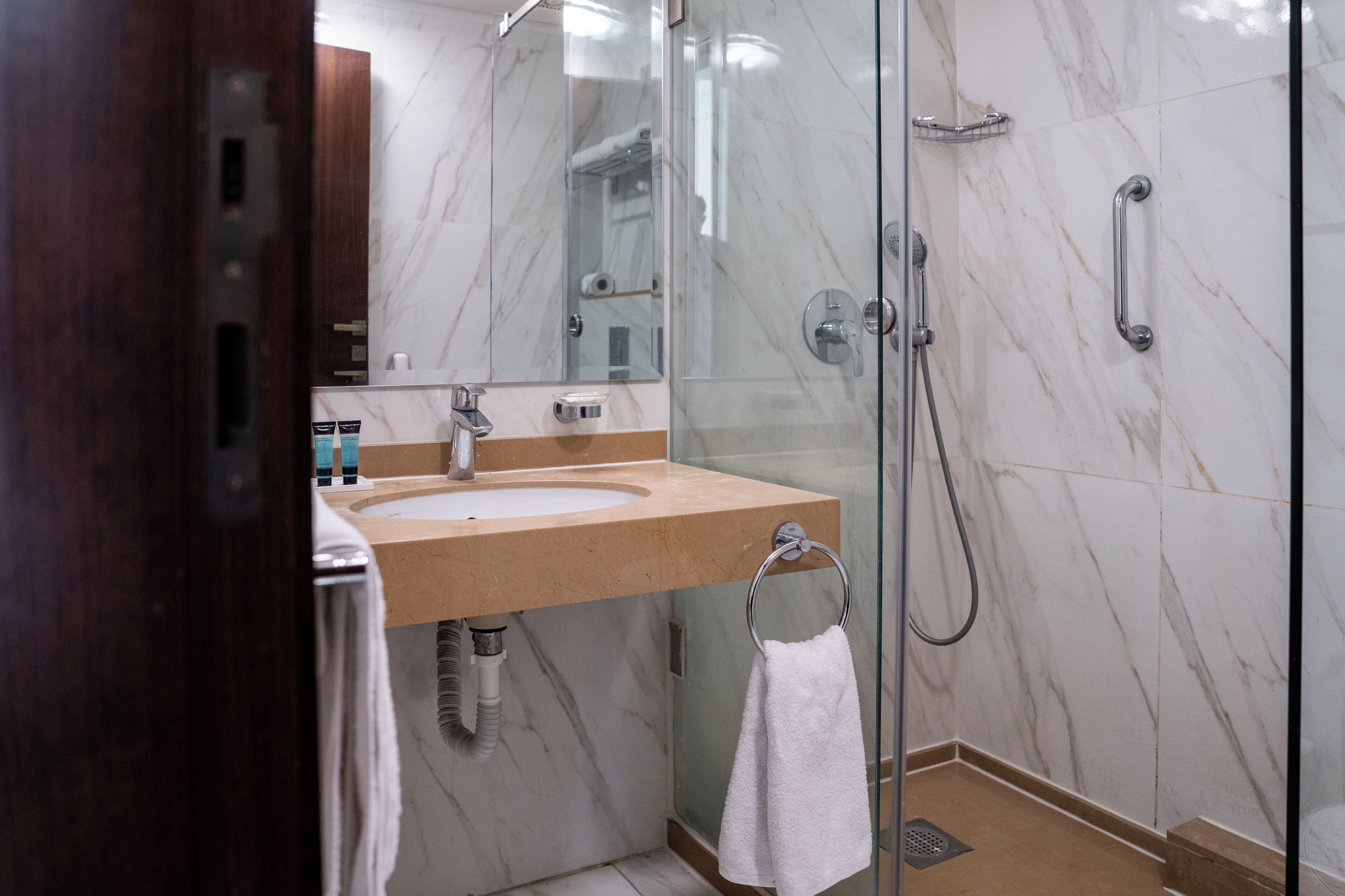A modern bathroom with a glass shower enclosure, a marble-tiled wall, and a wooden vanity.