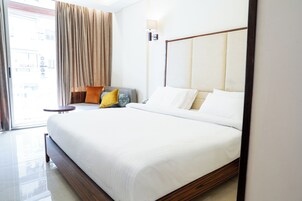 Habitación de hotel con una cama grande, una mesita de noche, una lámpara y vistas al exterior.