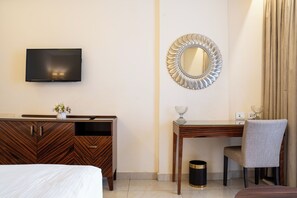 A hotel room with a bed, a wooden desk, a television, a mirror, and a chair.