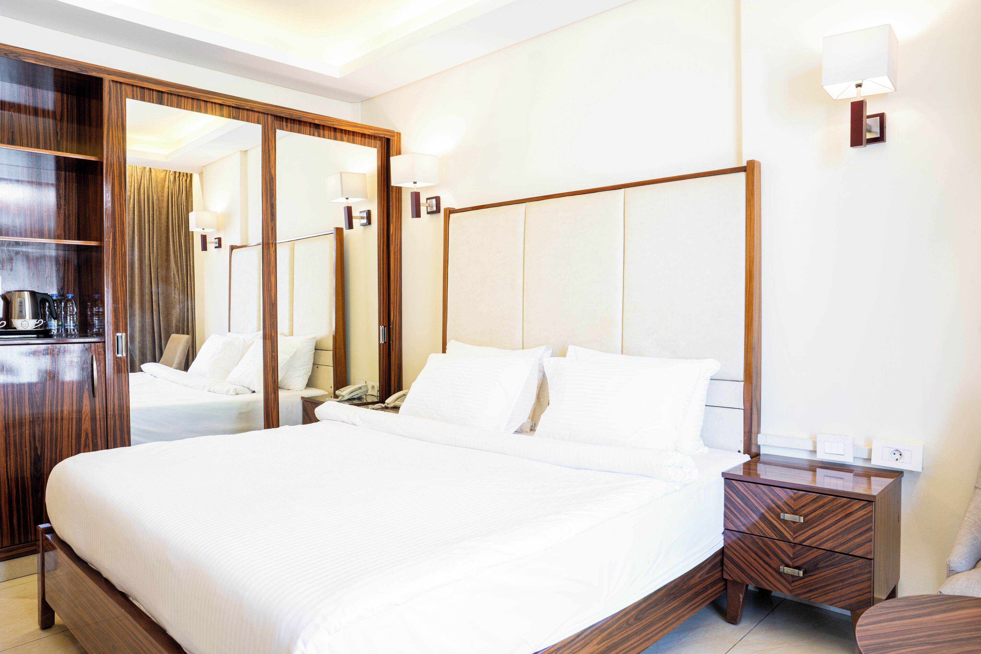 A hotel room with a large bed, wooden wardrobe, bedside table, and a mirror.