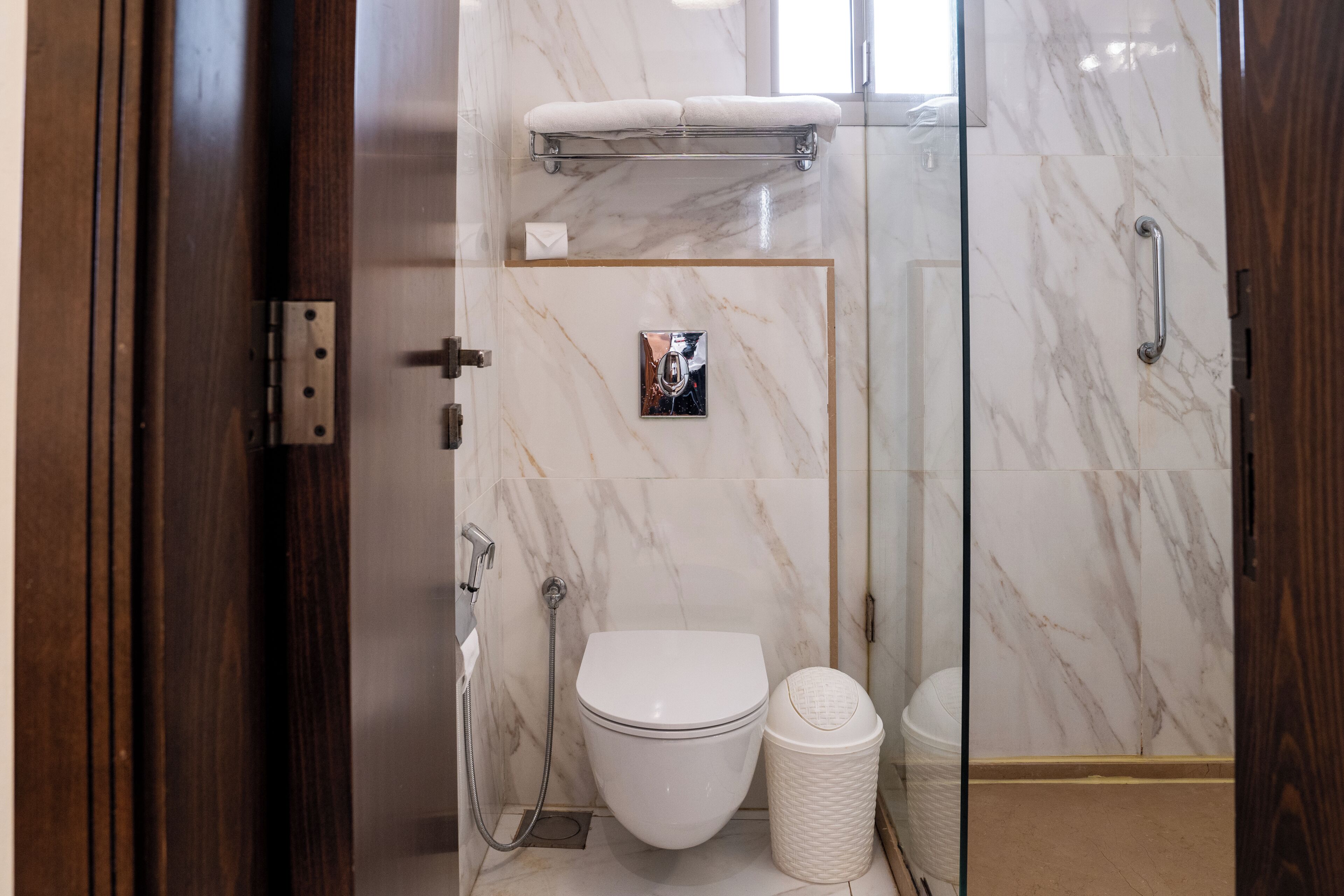 A modern bathroom with a glass shower enclosure, a white toilet, and a marble wall.
