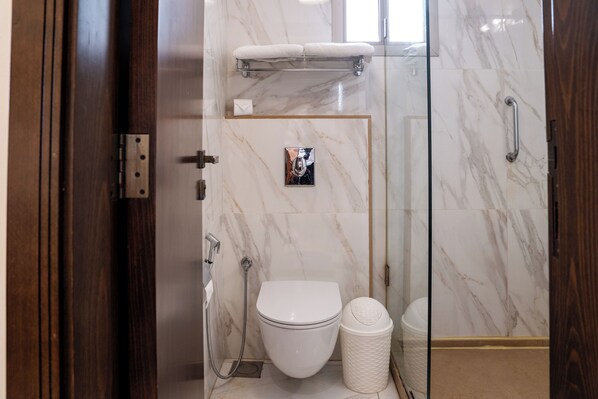A modern bathroom with a glass shower enclosure, a white toilet, and a marble wall.