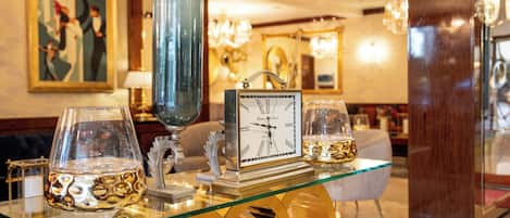 A glass-top table with a clock, decorative glasses, and a vase in a well-lit room with a chandelier.
