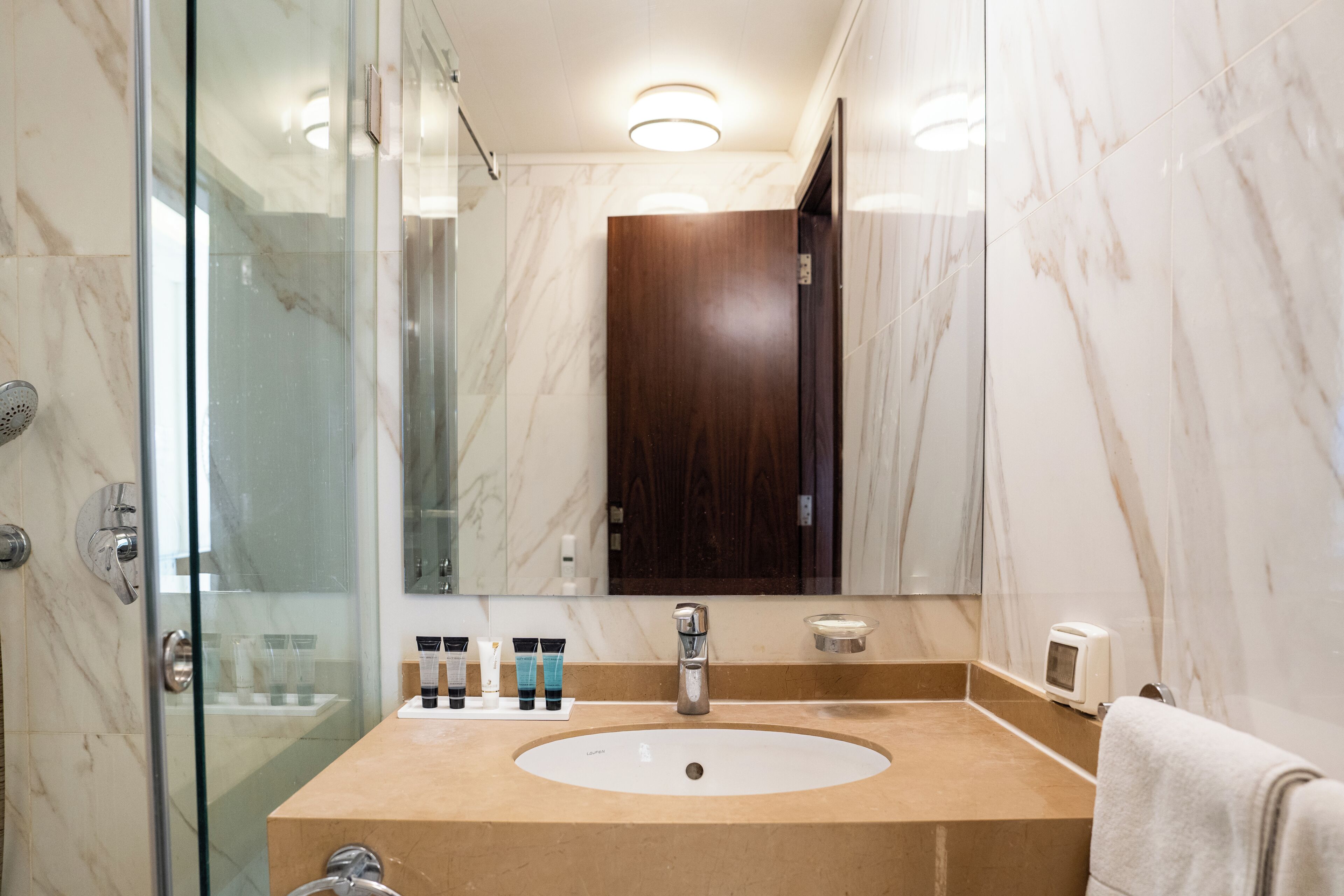 A bathroom with a marble sink, a glass shower enclosure, and a wooden door.
