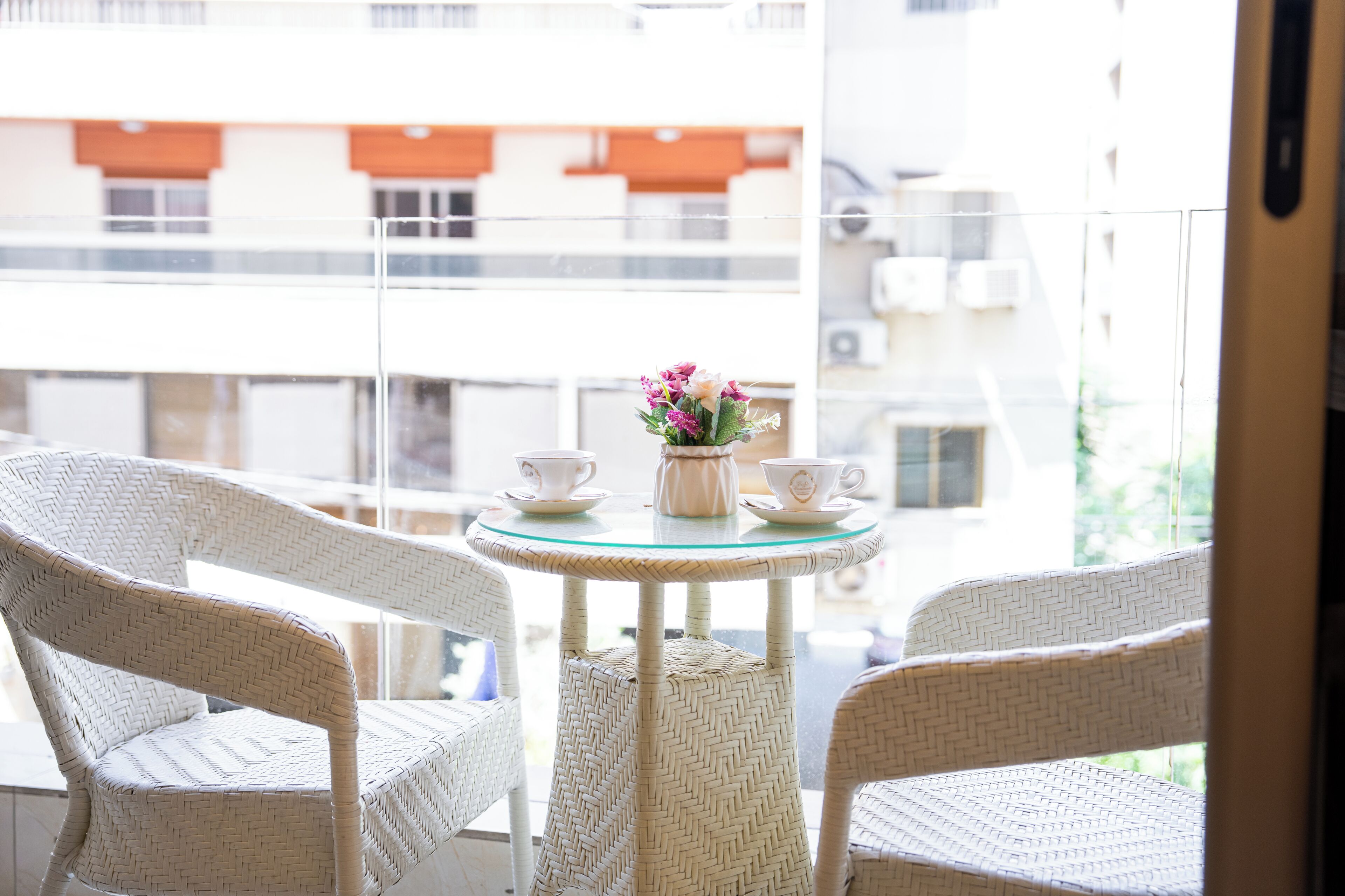 A balcony with wicker chairs, a glass table, and a vase with flowers.