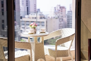 A balcony with wicker chairs, a small round table, and a vase of flowers.