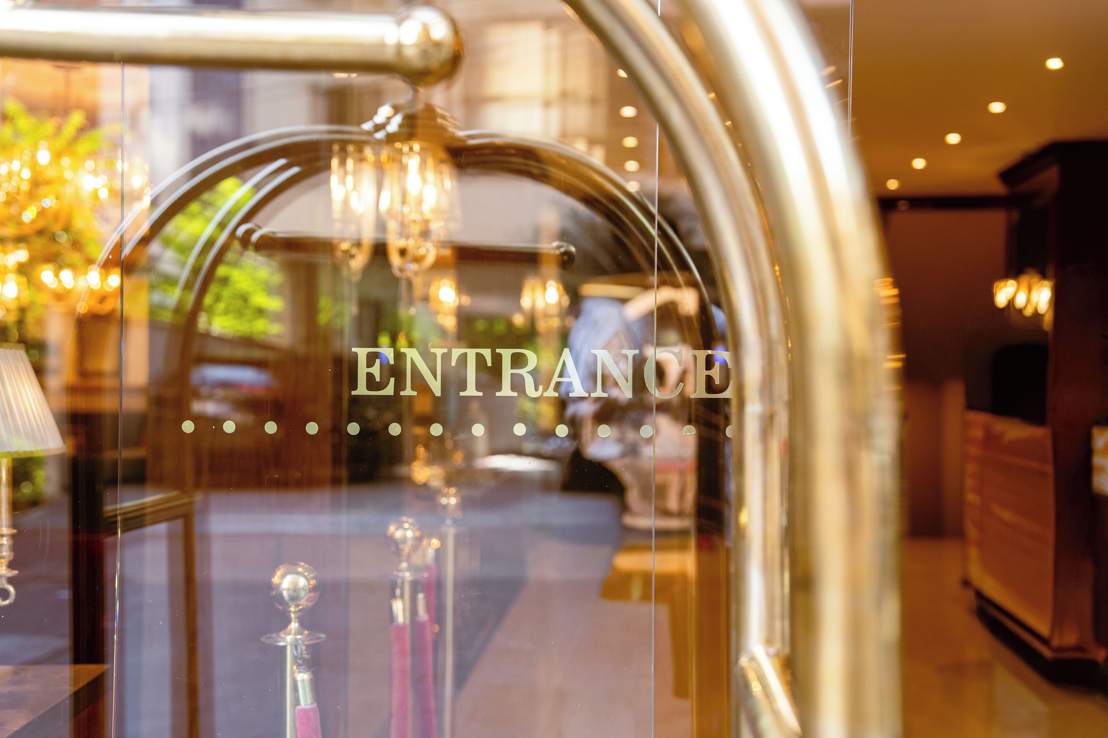 A glass door with the word 'ENTRANCE' and a reflection of a chandelier.