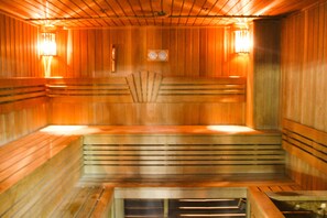 A sauna with wooden walls and benches, a sloped floor, and wall-mounted lights. - Belon Life Hotel (Astana)