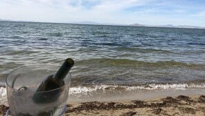 A glass with a bottle on a beach with waves and a distant mountain range. - Apartamentos Mar Menor (San Javier)