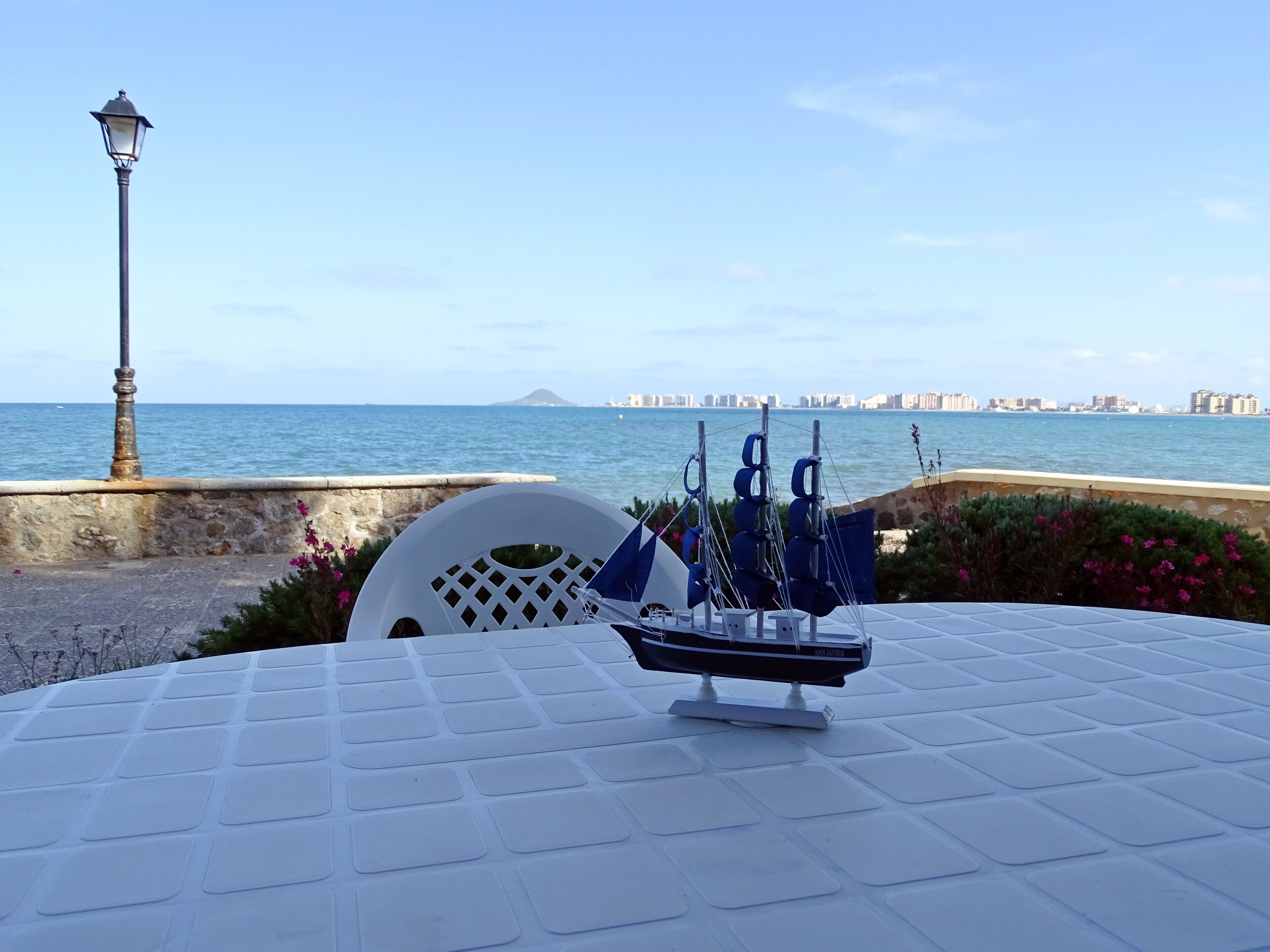 Vista al mar con una mesa, sillas, una lámpara y un barco modelo.