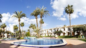 A resort with a swimming pool surrounded by palm trees and white buildings with red-tiled roofs. - Apartamentos Mar Menor (San Javier)