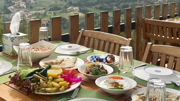 Mesa dispuesta para una comida con varios platos, un salero y un vaso de agua. La mesa está al aire libre con vistas a un paisaje de fondo.